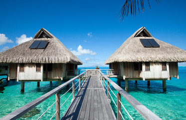 Wooden walkways over the water of the blue tropical sea to authentic traditional Polynesian thatched roof houses - 323532063