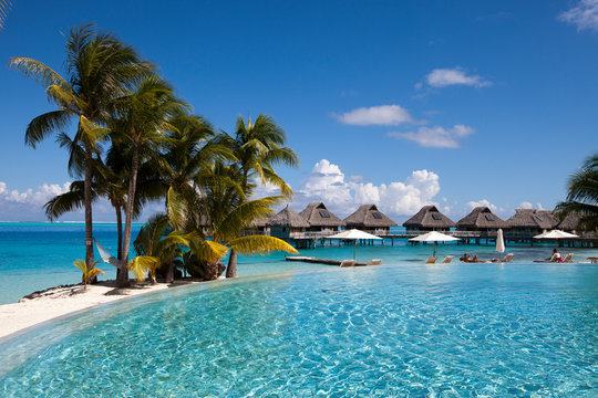 French Polynesia. Over water bungalows, sandy beach with palm trees and pool, Bora Bora..