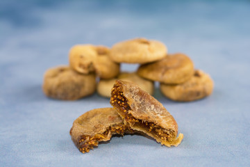 Dried figs. A mature common fig (Ficus carica) syconium in the front plane torn apart, showing its numerous one-seeded fruits. A few dried figs stacked in a blurry background. 