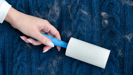 Woman hand using a sticky roller to clean fabrics - woolen knitted sweater from dust, hair, lint...