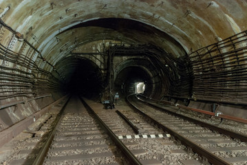 double-track reinforced concrete tunnel of the metro line.One of the railway lines turns of the right.The light is on.Electric high-voltage cables run along the walls of the tunnel   