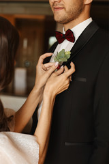 Close view of female hands fixing boutonniere on the jacket of a handsome man in a tuxedo and bow tie. Half face portrait of a stylish man in a wedding suit. Preparation of young groom