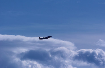 A jet plane climbing higher into the sky with puffy clouds