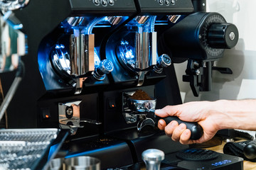 Close-up view of barista filling portafilter with fresh ground coffee under grinder