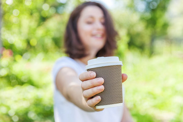 Fototapeta premium Happy girl smiling outdoor having lunch break. Beautiful young brunete woman with take away coffee cup resting on park or garden green background. Education freelancer resting leisure concept.