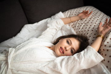 A beautiful caucasian girl in bed on a light background. Good morning.