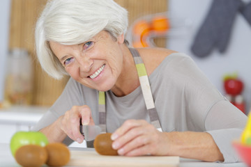 Obraz na płótnie Canvas senior woman cutting tomatoes in kitchen