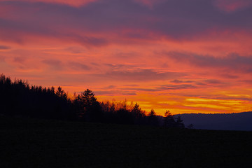 Landscape Picture of the dramatic or romantic red sky clouds over the deep forest or wood during the winter sunset in the highland part of Czech Republic. Beautiful part of country for holliday.