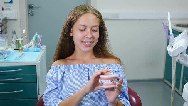 Smiling girl with orthopedic dental braces in dental chair. Healthcare, Dental Health and Dentistry concept. Happy Young Caucasian girl Looking at Camera Posing on dental office Background for Video