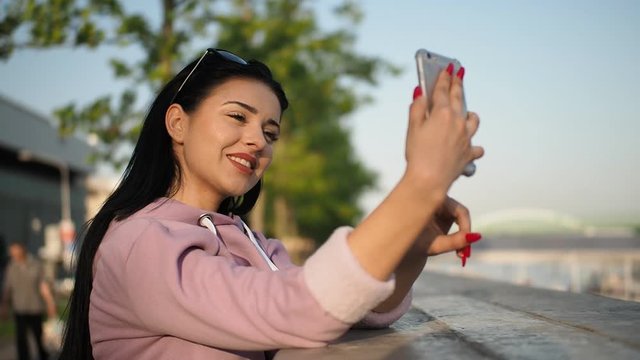 Young female tourist using smartphone in the bank of river Danube in Bratislava city for making selfies in HD VIDEO. Low depth of field and blurred background.