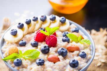 Healthy breakfast. Oatmeal porridge with berries, fruits and honey on dark background. Oatmeal with raspberries, blueberries and almonds on sackcloth. Top view