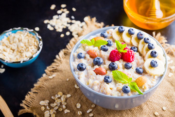 Healthy breakfast. Oatmeal porridge with berries, fruits and honey on dark background. Oatmeal with raspberries, blueberries and almonds on sackcloth. Top view