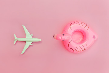 Summer beach composition. Minimal simple flat lay with plane and Inflatable flamingo isolated on pastel pink background. Vacation travel adventure trip concept. Top view copy space.
