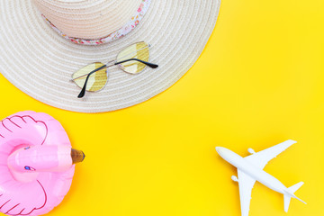 Summer beach composition. Minimal simple flat lay with plane sunglasses hat and Inflatable flamingo isolated on yellow background. Vacation travel adventure trip concept. Top view copy space.