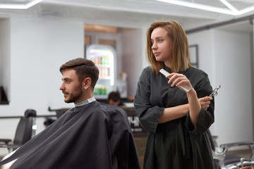 Handsome blue eyed man sitting in barber shop. Hairstylist Hairdresser Woman cutting his hair....