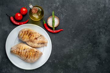 Grilled chicken fillet served in a white plate with spices on a stone background with copy space for your text.