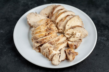 Sliced ​​- grilled chicken fillet, served in a white plate with spices, tomatoes, mustard on a stone background