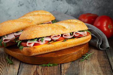 Two Long baguette Sandwiches with arugula, slices of fresh tomatoes, ham and cheese
