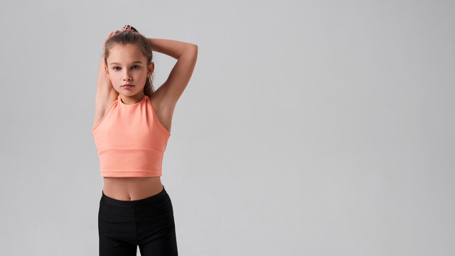 Fitter, healthier, happier. Flexible cute little girl child looking at camera while stretching her body isolated on a grey background. Sport, fitness, active lifestyle concept. Horizontal shot.