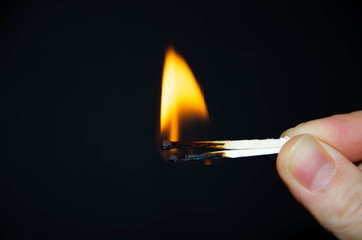 A hand holds a burning match on a black background. A wooden match burns in the hands of a macro....