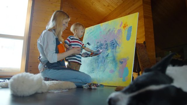  Little happy child colorful hands draw on canvas with mother together. Mom artist and her baby draw in the Studio.