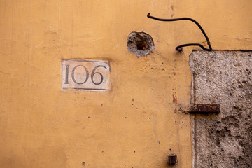 number 106, ancient house number plate on brick wall, Italy