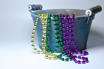 Colorful Mardi Gras bead necklaces draped on a wooden bucket with white background with copy space