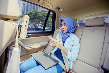 Muslim woman using mobile phone and laptop in car