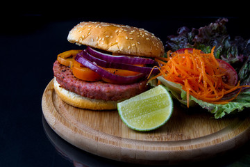 Hamburguesa de carne de atún con zanahoria, lechuga y limón. sobre tabla de madera y con una toma picada 
