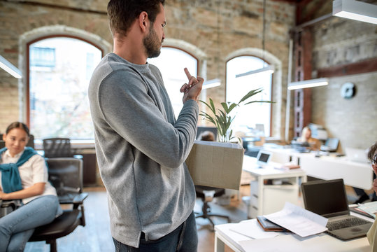 I hate you. Rude man in casual wear holding box with personal things and showing middle finger while leaving office