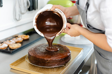 Patissier pouring liquid chocolate on a cake