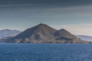 Ensenada, Mexico - January 17, 2012: Dark green mountain with antennas on top behind blue Pacific Ocean under light blue sky at entrance to All Saints Bay.