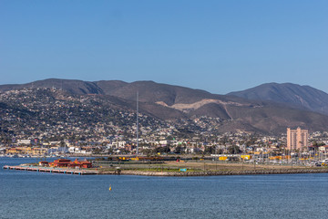 Ensenada, Mexico - January 17, 2012: Red Cruise Terminal at pier of harbor with cityscape on slope of mountain in back and behind blue bay water. Pink Villa Marina Hotel towers over all else.