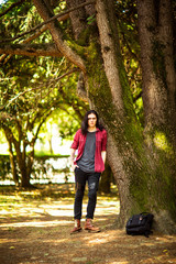 a young man with long hair,rock style, stands near a tree