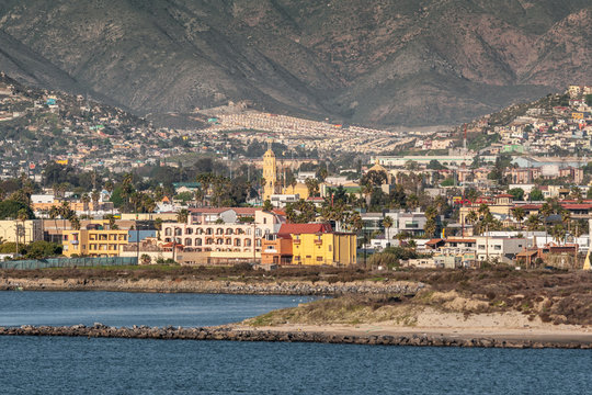 Ensenada, Mexico - January 17, 2012: Colored buildings on shoreline with towers of Cathedral of Lady of Guadelupe in back, surrounded by cityscape on slope of mountain.