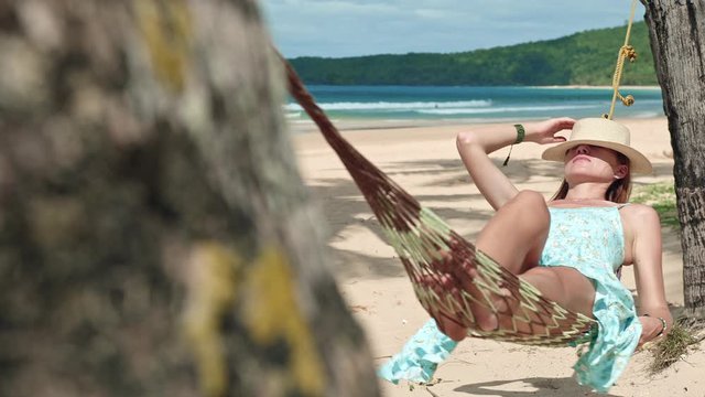 Travel concept - Beautiful young redhead vacation girl in hat and dress enjoying sea breeze in hammock on Nacpan beach, El Nido, Palawan, Philippines
