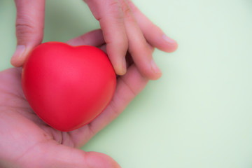 One hand puts a red heart shape in another hand, love and compassion concept