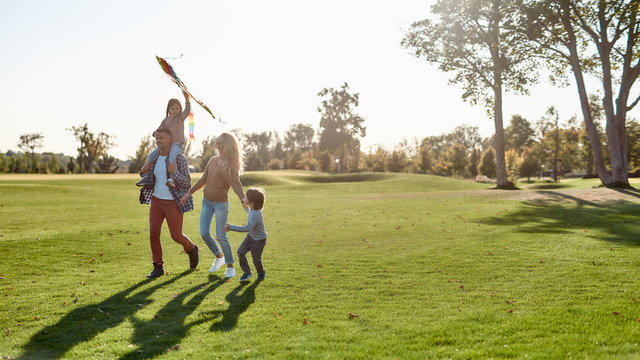 The First Happiness Of A Child To Know That He Is Loved. Happy Family Playing A Kite. Outdoor Family Weekend