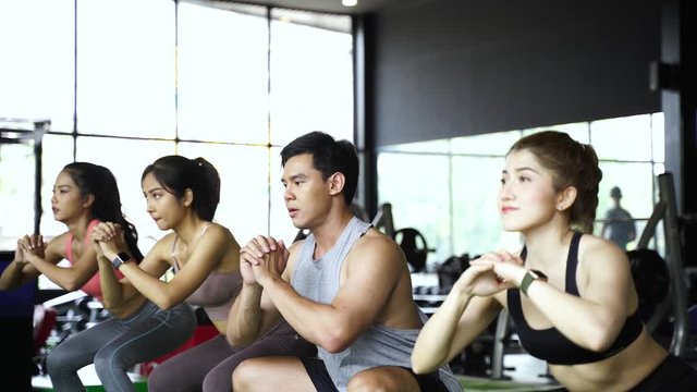Group of athletic young Asian people in sportswear doing squat and exercising at the gym. Intense workout and healthy lifestyle concept