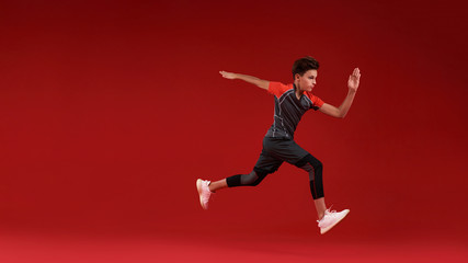 Fototapeta na wymiar Move. A teenage boy is engaged in sport, he is looking away while jumping. Isolated on red background. Fitness, training, active lifestyle concept. Horizontal shot