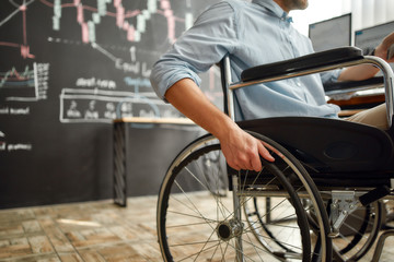Cropped photo of male office worker in a wheelchair working in the modern office. Disabled man holding a hand on wheel of a wheelchair while sitting at his workplace
