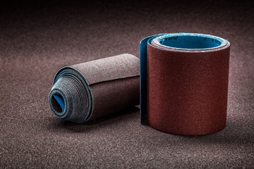 big rolls of abrasive paper on background of biggest sheet of sandpaper