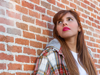 Peruvian girl with sunglasses on a sunset with brick wall in the background, checkered t-shirt and jeans.