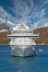 A white cruise ship anchored in a bay with people loading into lifeboats