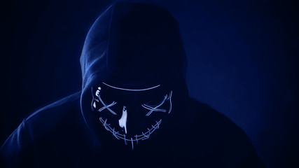 Man in scary lighting neon glow mask in hood in Phantom Blue color. Halloween and horror concept.