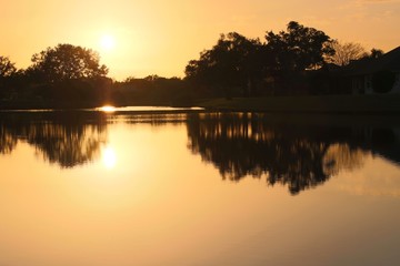 Fototapeta na wymiar Sunset casting orange glow over lake with reflections