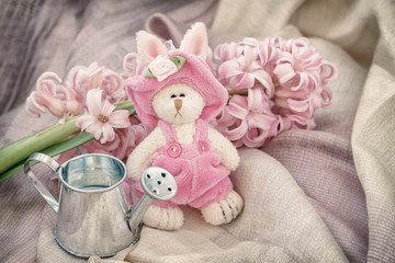 Pink bunnie with small garden watering can, spring flowers. Romantic still life. Gift on Valentin's, Mothers, Women's day. Tender vintage background.