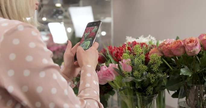 Happy woman florist photographs a ready-made bouquet on her phone in her flower shop
