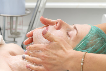 Beautician applies a natural moisturizing mask to the face of a young beautiful woman. Anti-aging...