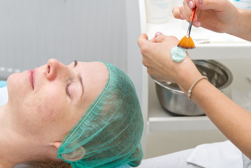 Beautician applies a natural moisturizing mask to the face of a young beautiful woman. Anti-aging...